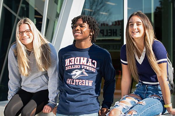 three Camden County College students laughing and smiling while standing in front of Taft building