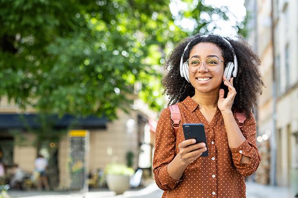 an African American woman listing to a podcast on her cellphone through headphones