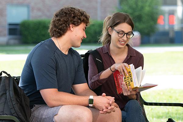 two students sitting on a bench reading a textbook